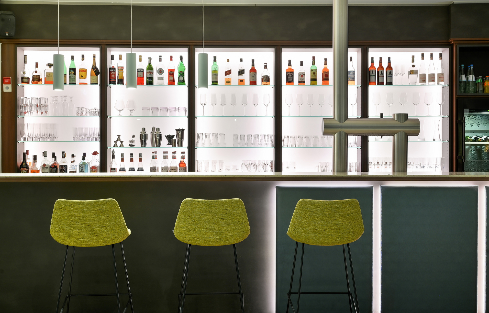 Eine stilvolle Bar mit einem beleuchteten Tresen und grünen Stühlen