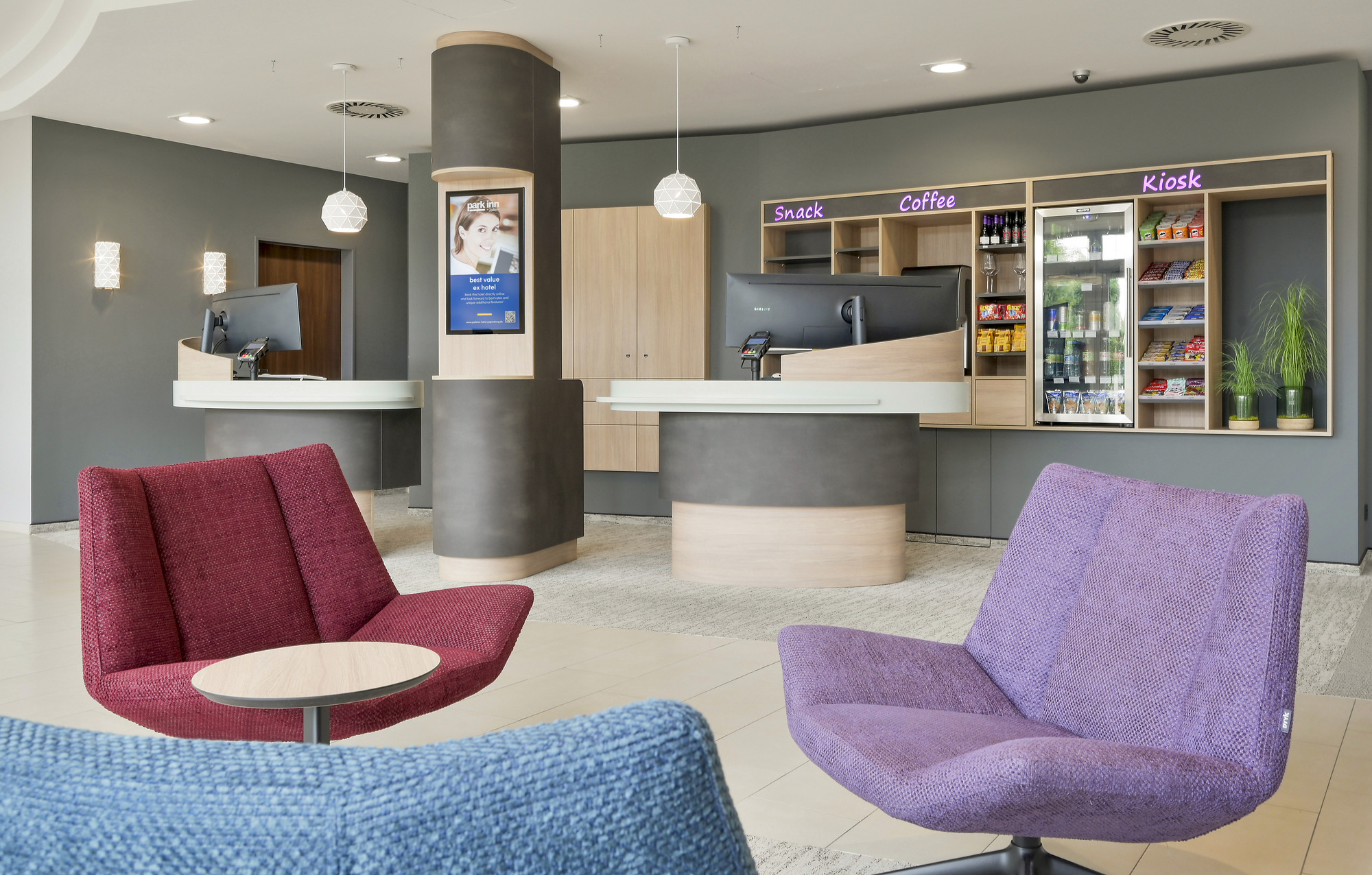 Moderne Hotellobby, die mit bunten Stühlen, einem Infoscreen und zwei Countern einladend und gemütlich gestaltet ist