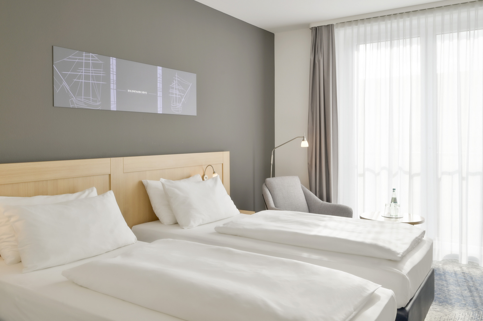 Helles Hotelzimmer mit zwei Betten, einem Stuhl und Tageslicht durch Fenster