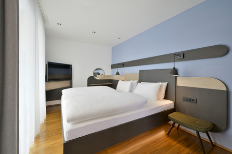 Modernes Schlafzimmer mit einem komfortablen Bett, stillvoller Beleuchtung, einem Fernseher und weißen Gardinen