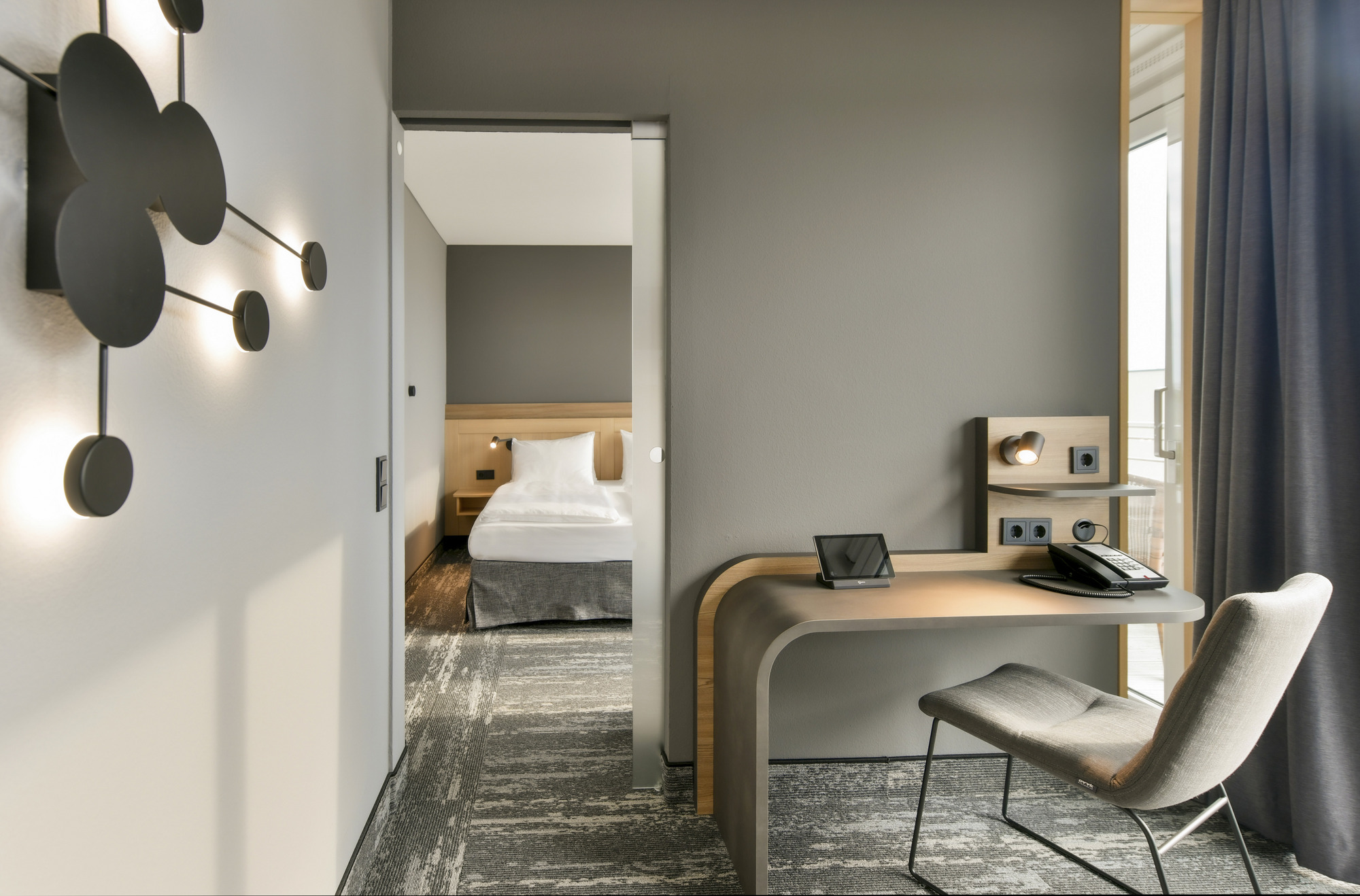 Helles, modernes Hotelzimmer mit elegantem Schreibtisch, bequemen Stuhl, schwarzer Lampe und separatem Schlafzimmer